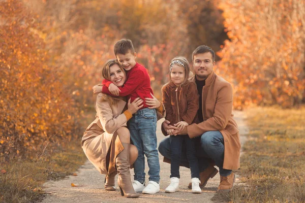 Familia feliz abrazándose en un paseo por el parque de otoño. Retrato de una madre y un padre caucásicos sosteniendo a sus hijos con hermosos trajes en un día soleado de otoño en el bosque. concepto de estilo de vida familiar. —  Fotos de Stock