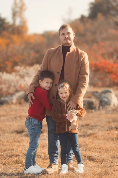 Ritratto di un padre caucasico che abbraccia i suoi figli in splendidi abiti in una soleggiata giornata autunnale nel parco naturale. Concetto felicità familiare. — Foto Stock