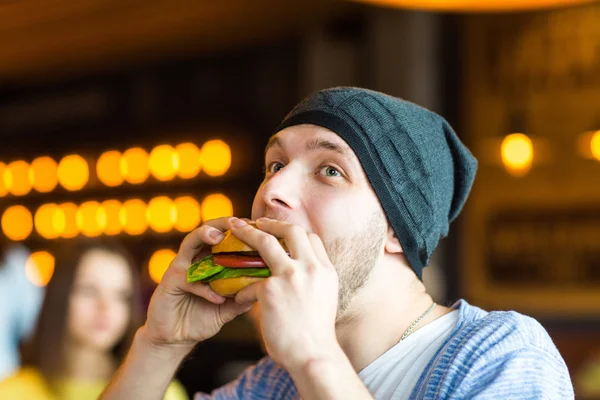 Man in hands holds a burger. Man eating a burger at the cafe — Stock Photo, Image