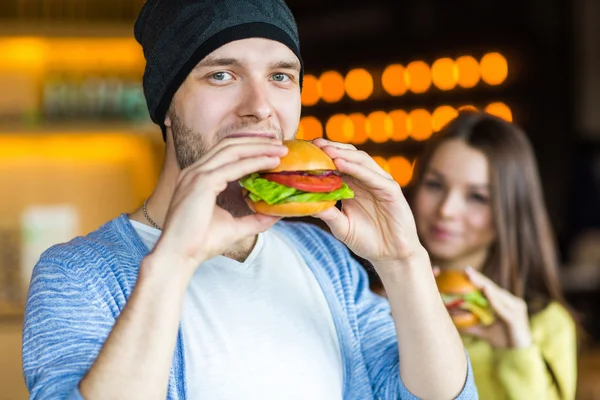 Man and woman eating burger. Young girl and young man are holding burgers on hands