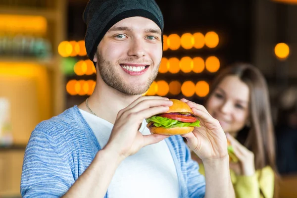 Man and woman eating burger. Young girl and young man are holding burgers on hands