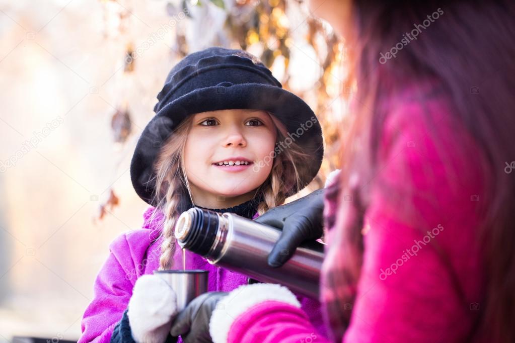 mother-child pours tea or coffee from a thermos in autumn in the park. Mom daughter pours coffee or tea from a thermos