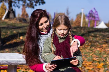 Anne ve kızı sonbahar parkta bir bankta tablet ile. Anne ve kızı parkta