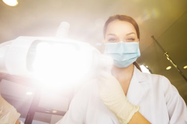 young women dentist with sterile mask readily approaching a patient with dental instruments held in the hands protected with surgical gloves young dentist with sterile mask