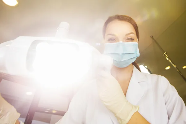 Mulheres jovens dentista com máscara estéril prontamente se aproximando de uma paciente com instrumentos odontológicos mantidos nas mãos protegidas com luvas cirúrgicas dentista jovem com máscara estéril — Fotografia de Stock