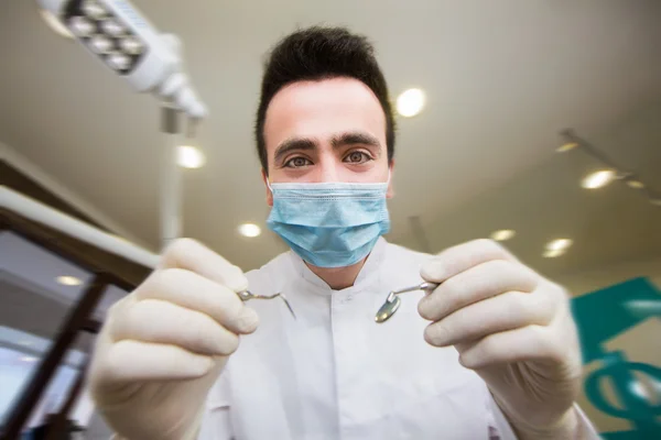 Joven odontólogo con máscara estéril se acerca fácilmente a un paciente con instrumentos dentales en las manos protegidos con guantes quirúrgicos joven odontólogo con máscara estéril —  Fotos de Stock