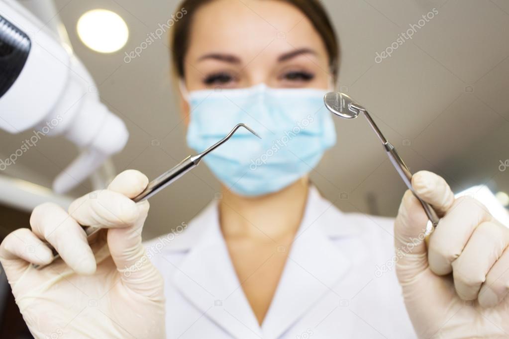 young women dentist with sterile mask readily approaching a patient with dental instruments held in the hands protected with surgical gloves young dentist with sterile mask
