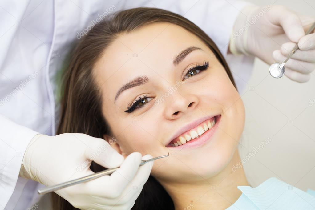 Close-up of young woman during inspection of oral cavity with help of hook and mirror
