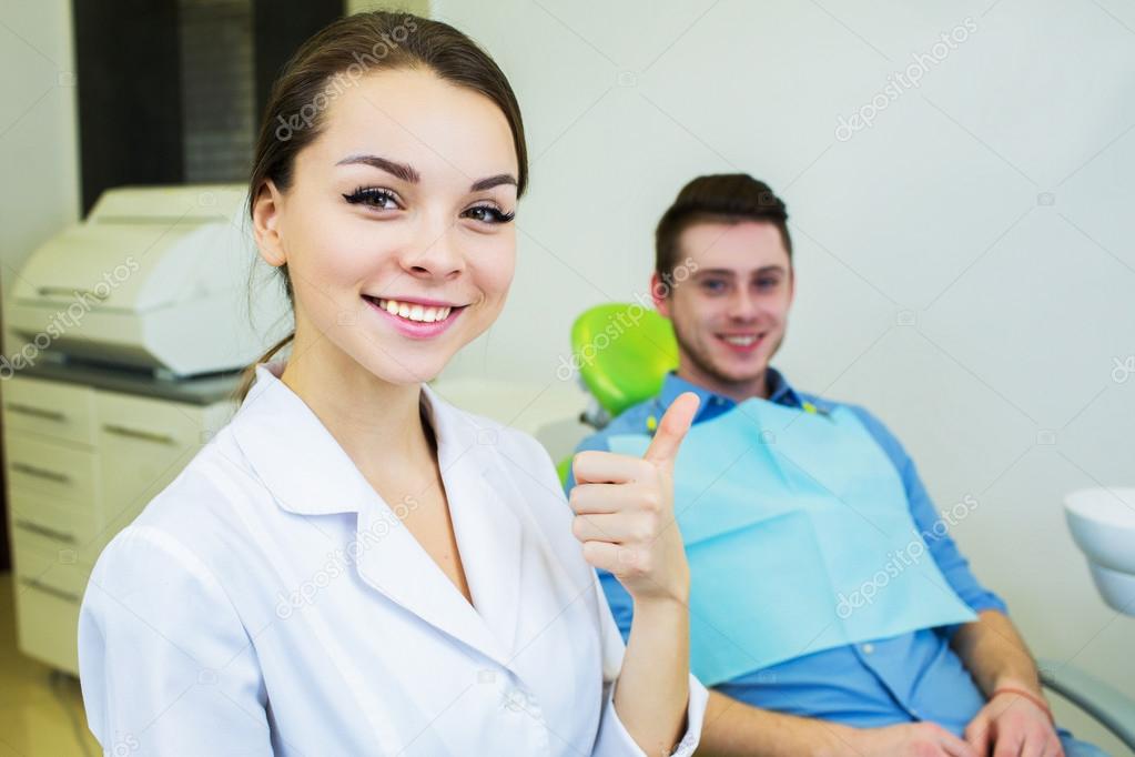 Dental surgeon and patient smiling happy after dental checkup, looking at camera.