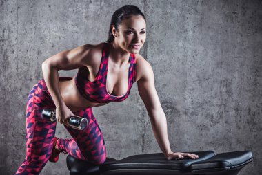 Gri bir arka plan üzerinde dumbbells ile egzersiz yaparak güzel kaslı kadın. Arka plan beton duvar