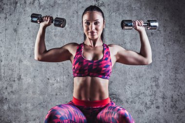 Gri bir arka plan üzerinde dumbbells ile egzersiz yaparak güzel kaslı kadın. Arka plan beton duvar