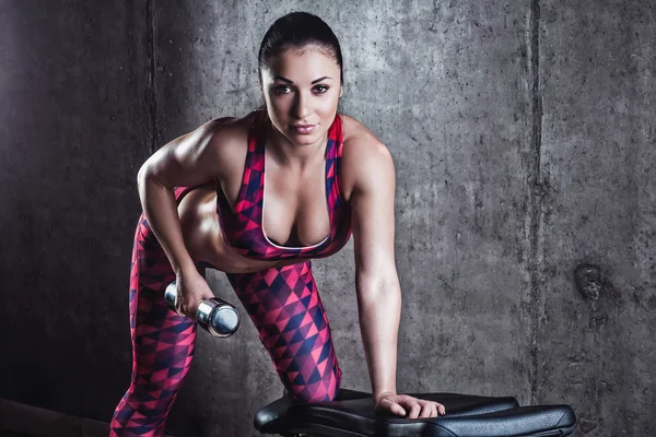 Gri bir arka plan üzerinde dumbbells ile egzersiz yaparak güzel kaslı kadın. Arka plan beton duvar