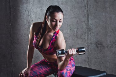 Gri bir arka plan üzerinde dumbbells ile egzersiz yaparak güzel kaslı kadın.