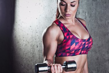 Gri bir arka plan üzerinde dumbbells ile egzersiz yaparak güzel kaslı kadın.