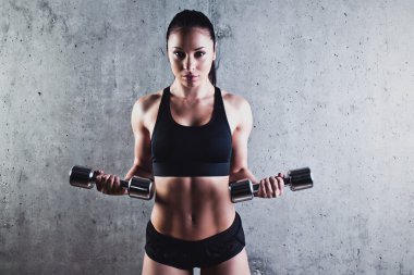 Gri bir arka plan üzerinde dumbbells ile egzersiz yaparak güzel kaslı kadın.
