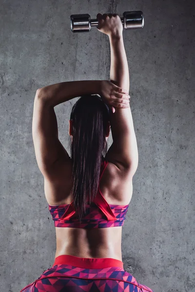 Piękna kobieta mięśni robi ćwiczenia z hantlami na szarym tle. — Zdjęcie stockowe