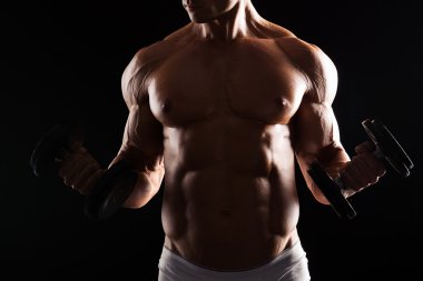 Güçlü atletik kas vücut siyah arka plan üzerinde gösterilen adam. Kaslı vücut geliştirmeci adam dumbbells ile siyah arka plan üzerinde yapıyor. Kaslı adam siyah arka plan üzerine