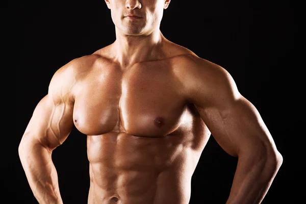 Hombre atlético fuerte mostrando el cuerpo muscular sobre un fondo negro.Hombre musculoso sobre fondo negro — Foto de Stock