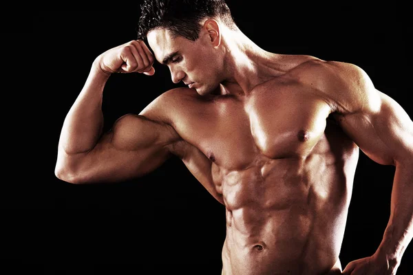 Homem Atlético Forte mostrando corpo muscular em um fundo preto.Homem muscular em fundo preto — Fotografia de Stock