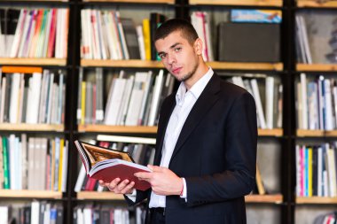 Öğrenci Kitaplığı'nda. kitap tutan ve kitaplıktaki dururken gülümseyen yakışıklı delikanlı