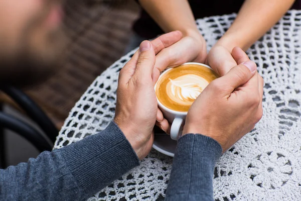 Quatro mãos enroladas em torno de uma xícara de café — Fotografia de Stock