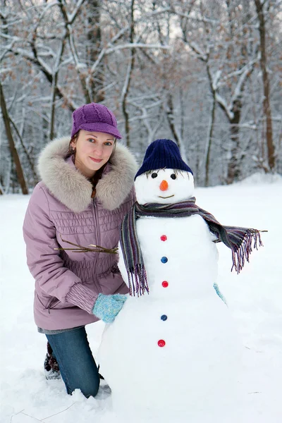 Mooi meisje in de buurt van een sneeuwpop — Stockfoto