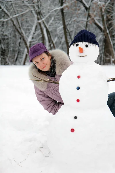 Mooi meisje in de buurt van een sneeuwpop — Stockfoto