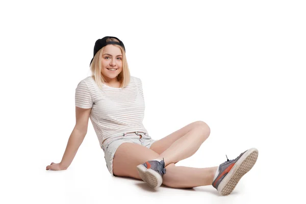 Sonriente chica usando camiseta y pantalones cortos de jean sentado en el suelo aislado —  Fotos de Stock