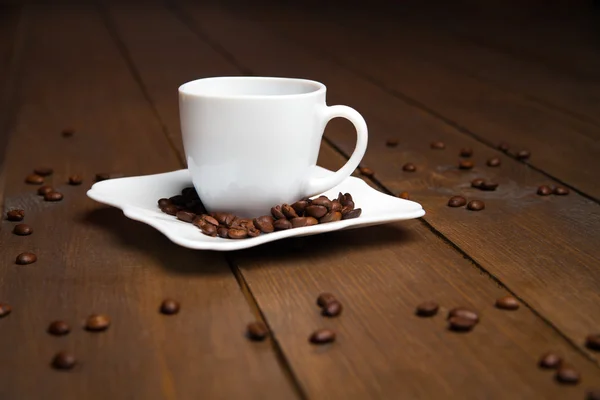 Aromatische koffie in witte kopje met schotel en verspreide bonen — Stockfoto