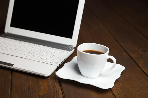 Verse zwarte koffie in cup op schotel in de buurt van laptop — Stockfoto