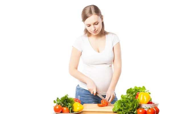 Pregnant woman cutting tomato in studio — Stock Photo, Image