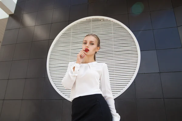 Attractive model in blouse and skirt looking away against of geometric modern building wall — Stock Photo, Image