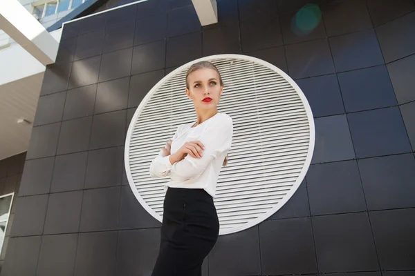 Modelo atractivo en blusa y falda mirando hacia otro lado de la pared del edificio moderno geométrico —  Fotos de Stock