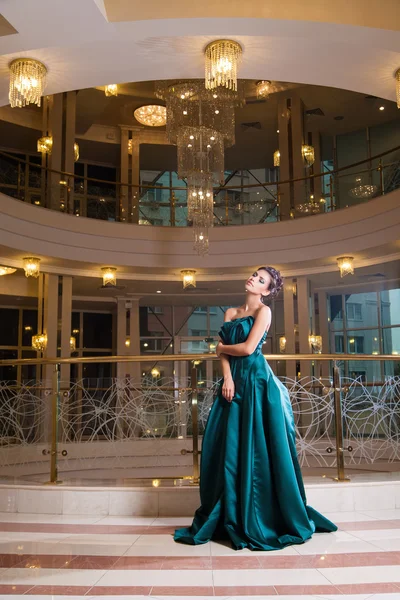 Elegant modell i vacker grön klänning poserar mot av belysta ljuskrona — Stockfoto