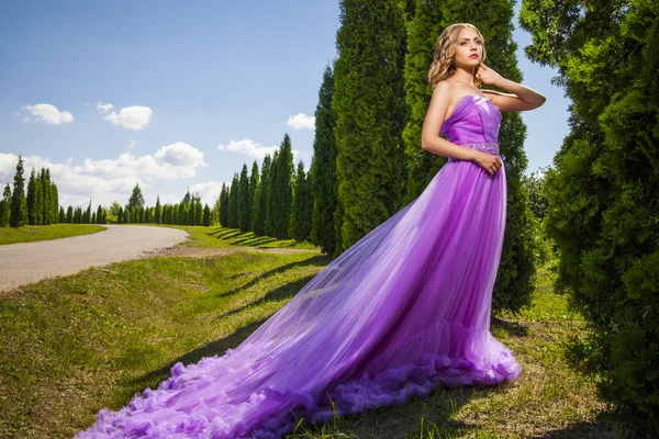 Elegante mujer en vestido largo violeta contra de callejón verde —  Fotos de Stock