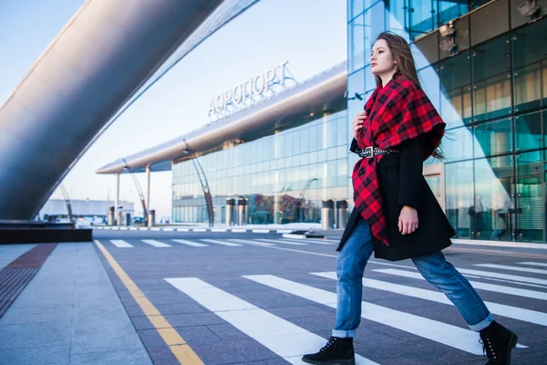 Mujer joven caminando a través del cruce peatonal contra el edificio del aeropuerto —  Fotos de Stock