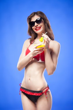 Mavi arka plan karşı içki tutan güneş gözlüğü ince bikini modeli