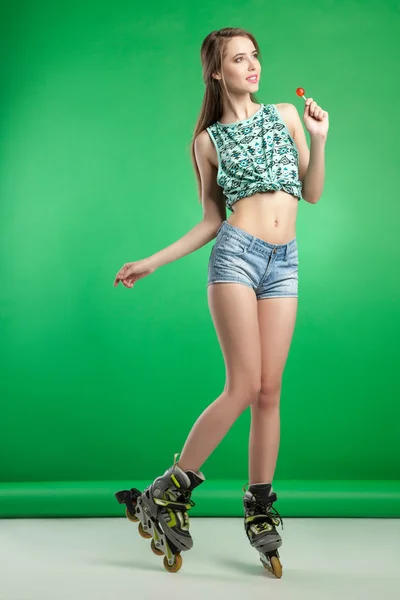 Zeer aantrekkelijke vrouw met lolly poseren op groene studio achtergrond dragen rollerskates — Stockfoto