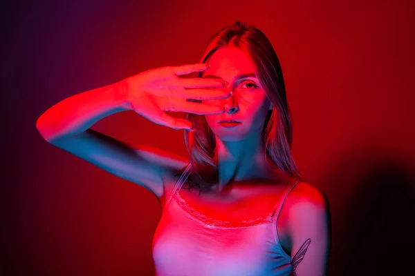 Неемоційна молода жінка покриває очі рукою в студії з червоним світлом — стокове фото