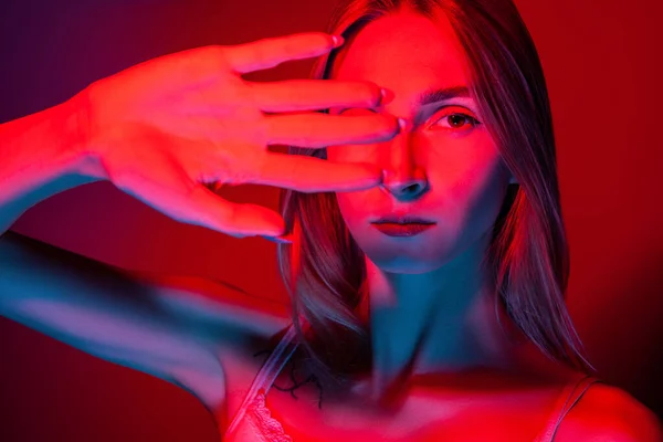 Niewzruszona młoda kobieta okrywająca oczy dłonią w studiu czerwonym światłem — Zdjęcie stockowe
