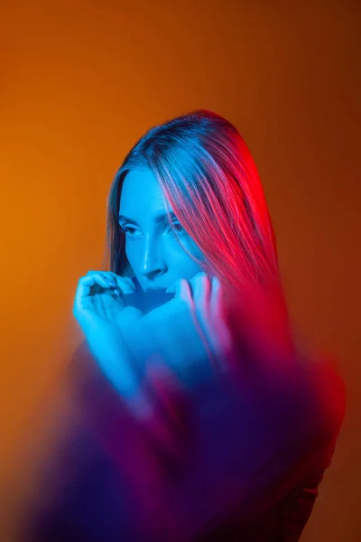 Jeune femme réfléchie avec lumière bleue sur le visage dans un studio orange — Photo