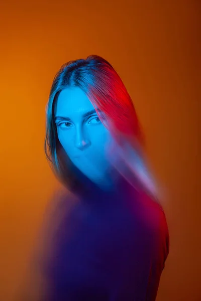 Przemyślana młoda dama z niebieskim światłem na twarzy w pomarańczowym studio — Zdjęcie stockowe