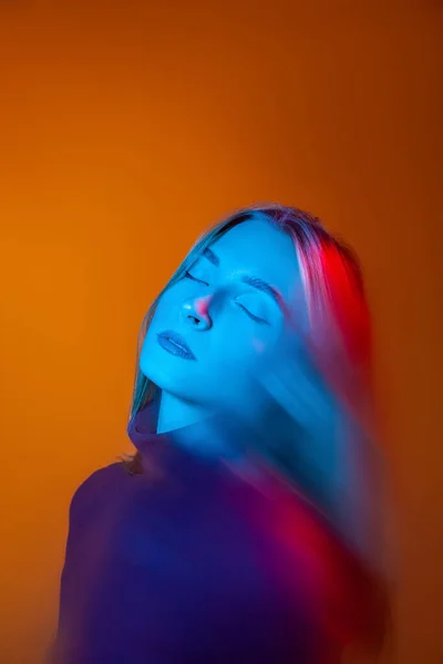 Προσεκτική νεαρή κοπέλα με μπλε φως στο πρόσωπο σε πορτοκαλί στούντιο — Φωτογραφία Αρχείου