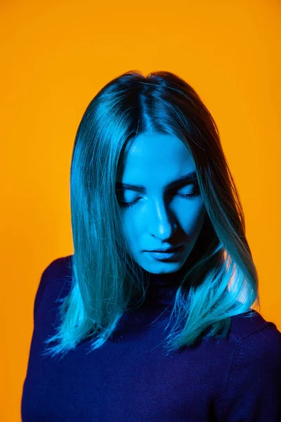 Pensive młoda kobieta z zamkniętymi oczami w jasnym studio z niebieskim oświetleniem — Zdjęcie stockowe