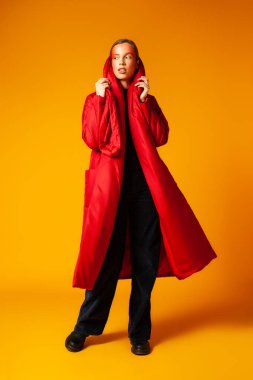 Kadın model sarı arkaplana karşı kırmızı ceketi ayarlıyor