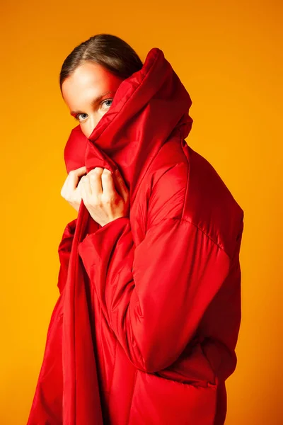 Молода жінка, обгорнута червоним пальто на жовтому тлі — стокове фото