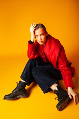 Yalnız bir kadın sarı arka planda bol bir paltoya sarılıyor.