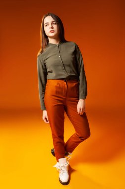 Son moda genç kadın turuncu arka planda kameraya bakıyor.