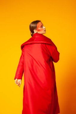 Sarı arka planda parlak kırmızı ceketli kadın model.