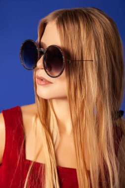 Mavi arka planda kendine güvenen, modaya uygun giyinmiş genç bir kadın.